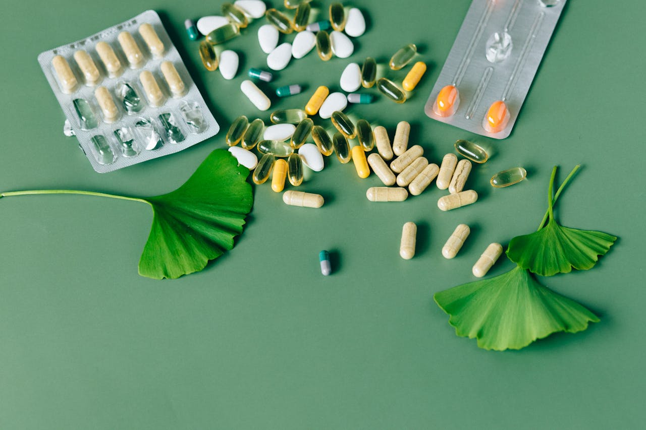 A variety of natural supplements and pills displayed on a green background with Ginkgo biloba leaves.
