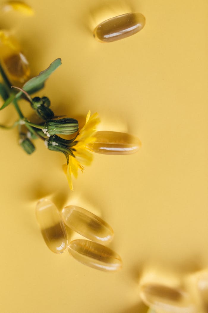 Yellow softgels and dandelion flower on a vibrant yellow surface, representing natural supplements.